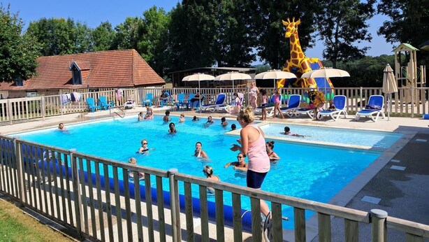 Ein Schwimmbecken mit Schwimmern und Liegebädern, umgeben von einem Holzzaun und beschattet durch Sonnenschirme.