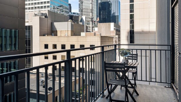 Balcón con una mesa y una silla, con vista a un paisaje urbano con diversos edificios.
