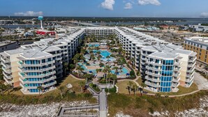 Ein Resort mit mehreren Gebäuden, einem zentralen Poolbereich und einem Strand im Vordergrund.
