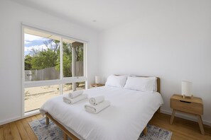 A bedroom with a large window, a bed with white linens, two bedside tables, and a view of the outdoors. - Peaceful 2-Bed Apartment in Coastal McCrae (McCrae)
