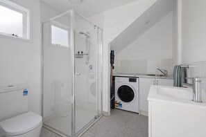Casa de banho compacta com chuveiro envidraçado, máquina de lavar roupa e lavatório.