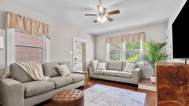 Ein Wohnzimmer mit zwei Sofas, einem Holztisch, einem Deckenventilator und einem großen Fenster mit Vorhängen.