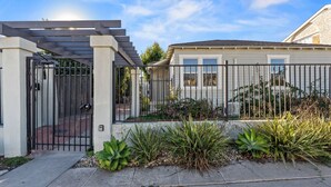 A gated residential area with a covered entryway, a house with a light-colored exterior, and a well-maintained garden with various plants.