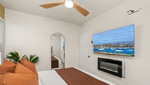 A hotel room with a bed, a ceiling fan, a TV mounted on the wall, and a view of a marina.
