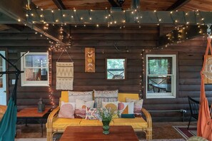 A cozy cabin interior with a sofa, hanging lights, and a wooden wall.