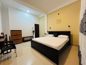 A bedroom with a large bed, a desk, a chair, a radiator, and a door. - Hidden Gem - Goyambokka (Tangalle)