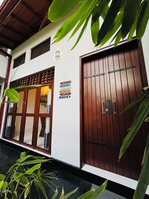 A building with a large wooden door and windows, a sign reading "Welcome to our home," and a small sign with various phrases. - Hidden Gem - Goyambokka (Tangalle)