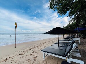 A beach with sun loungers and umbrellas, a flag, and footprints in the sand. - Hidden Gem - Goyambokka (Tangalle)