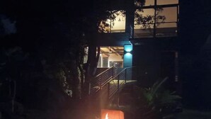 Szenenacht mit einem beleuchteten Außenfeuerkorb, einer Treppe, die zu einem Gebäude führt, und einer sichtbaren Tür.