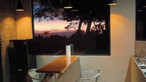 Ein Essbereich mit Holztisch und zwei Korbstühlen, einem großen Fenster mit Sonnenuntergangsblick und Pendelleuchten.