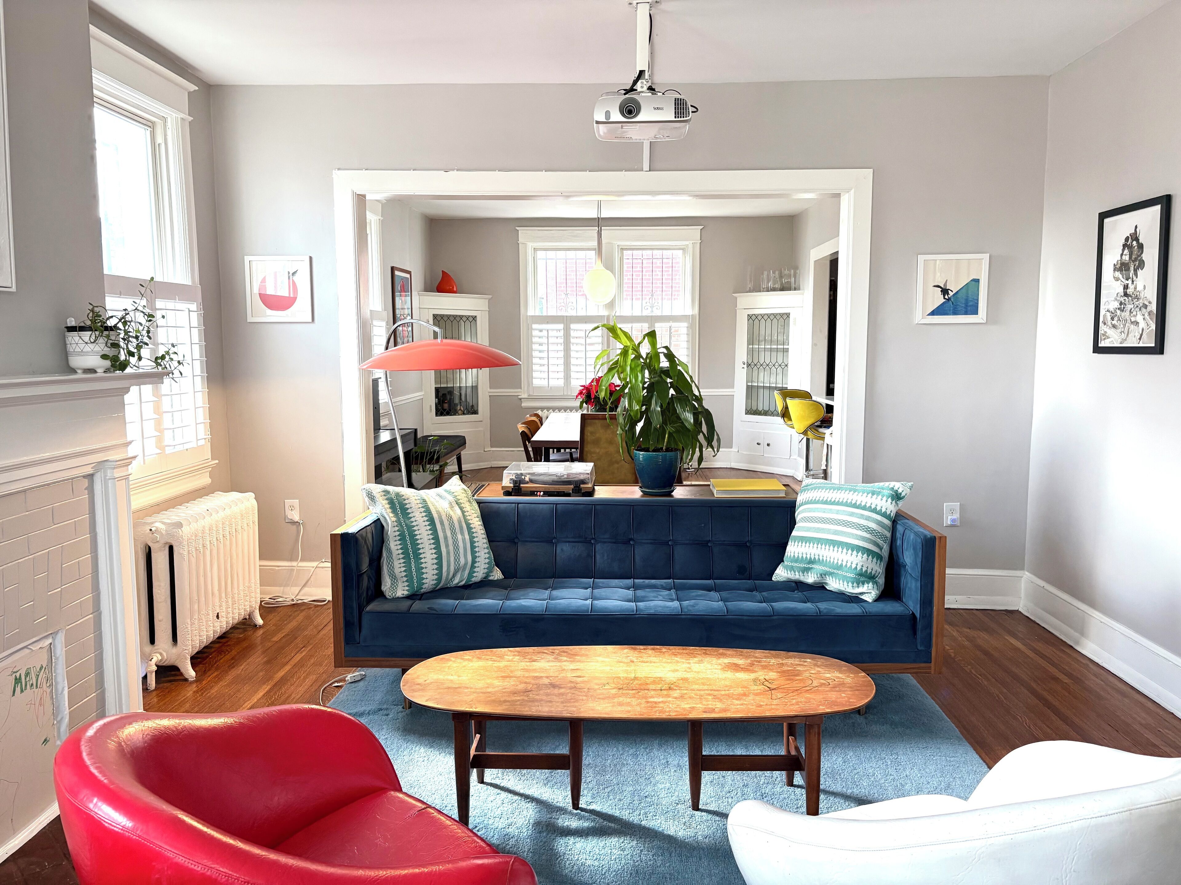 A living room with a blue sofa, a red chair, a wooden coffee table, and a white armchair.
