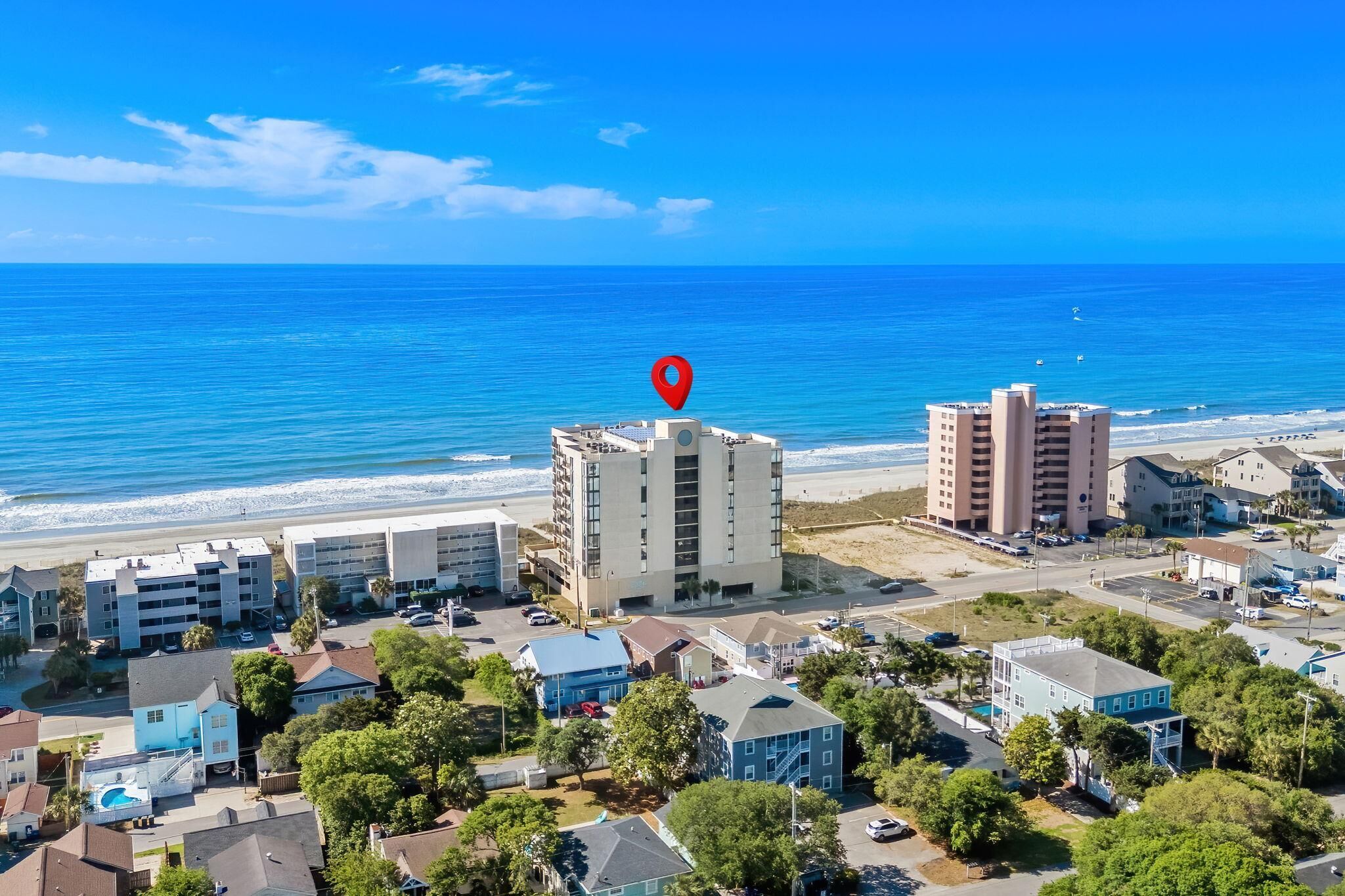 A coastal hotel with multiple buildings, a beach view, and a red location marker.