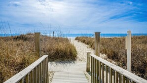 A wooden boardwalk leading to the beach, surrounded by tall grasses and a clear blue sky. - Beachfront Breeze @ Sea Castle North Myrtle Beach (North Myrtle Beach)