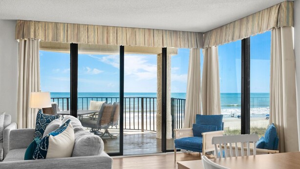 A hotel room with a balcony, a sofa, a table, and a view of the beach. - Beachfront Breeze @ Sea Castle North Myrtle Beach (North Myrtle Beach)