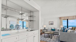 A modern kitchen with a large island, a dining area with a sofa and table, and a view of the sea. - Beachfront Breeze @ Sea Castle North Myrtle Beach (North Myrtle Beach)