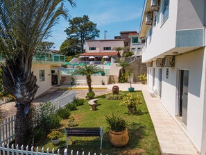 A courtyard with a white fence, a bench, potted plants, and a palm tree. - Hotel Pousada Delplata (Serra Negra)