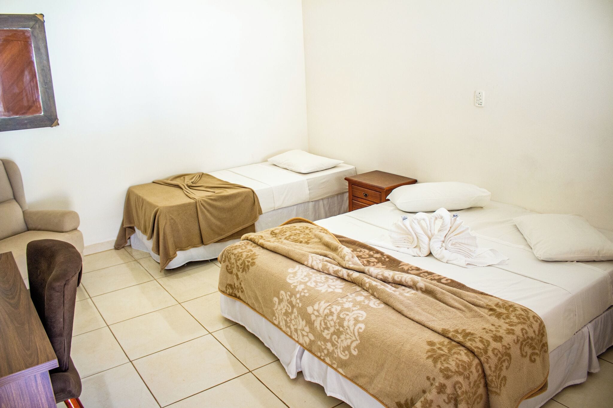 Una habitación de hotel con dos camas individuales, una mesita de noche de madera, una silla y una pequeña mesa.