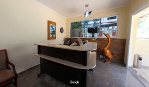 A reception desk with a wooden chair, a clock on the wall, and a window with a view of the outside. - Hotel Pousada Delplata (Serra Negra)