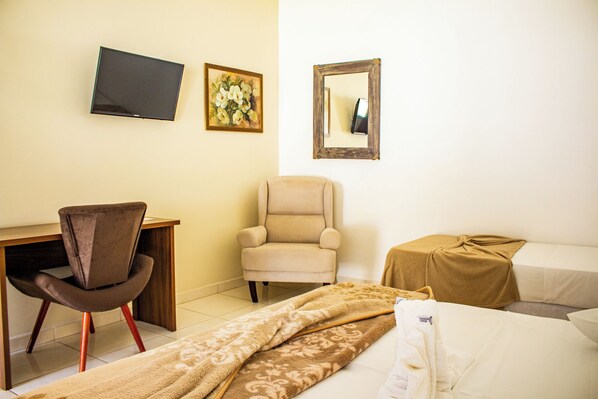 Una habitación de hotel con escritorio, una silla, una cama, televisor y espejo.