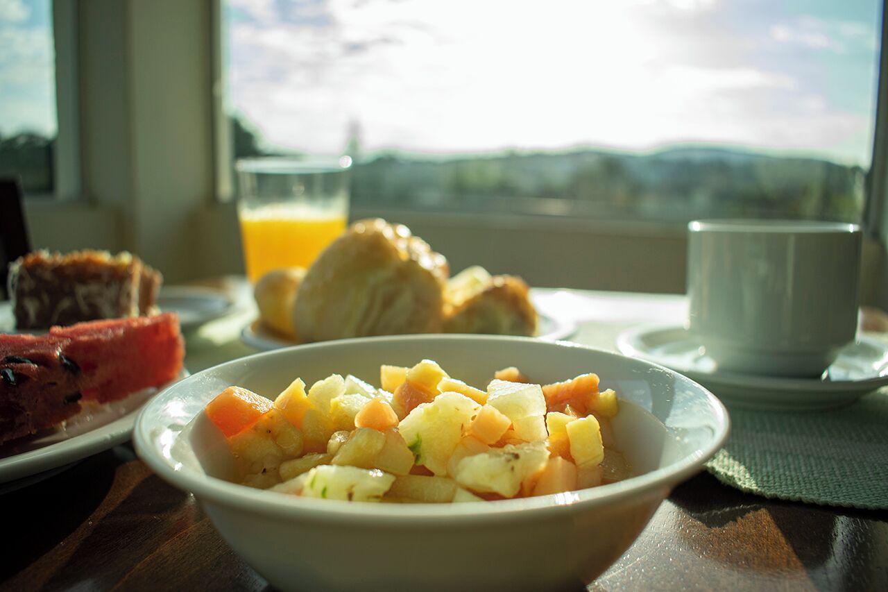 Une table dressée pour le petit-déjeuner, avec un saladier de fruits frais, des croissants et un verre de jus d’orange, placée près d’une fenêtre donnant sur le paysage extérieur.
