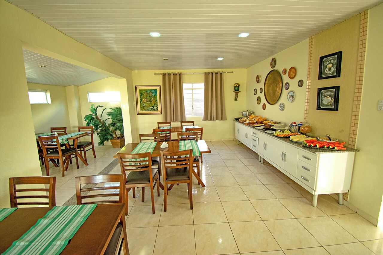 A dining area with wooden tables and chairs, a buffet counter with food, and a wall decorated with plates and a painting.