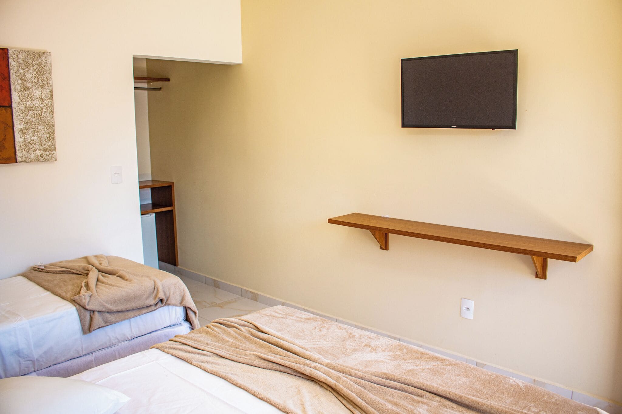 A bedroom with two beds, a mounted TV, and a wooden shelf.