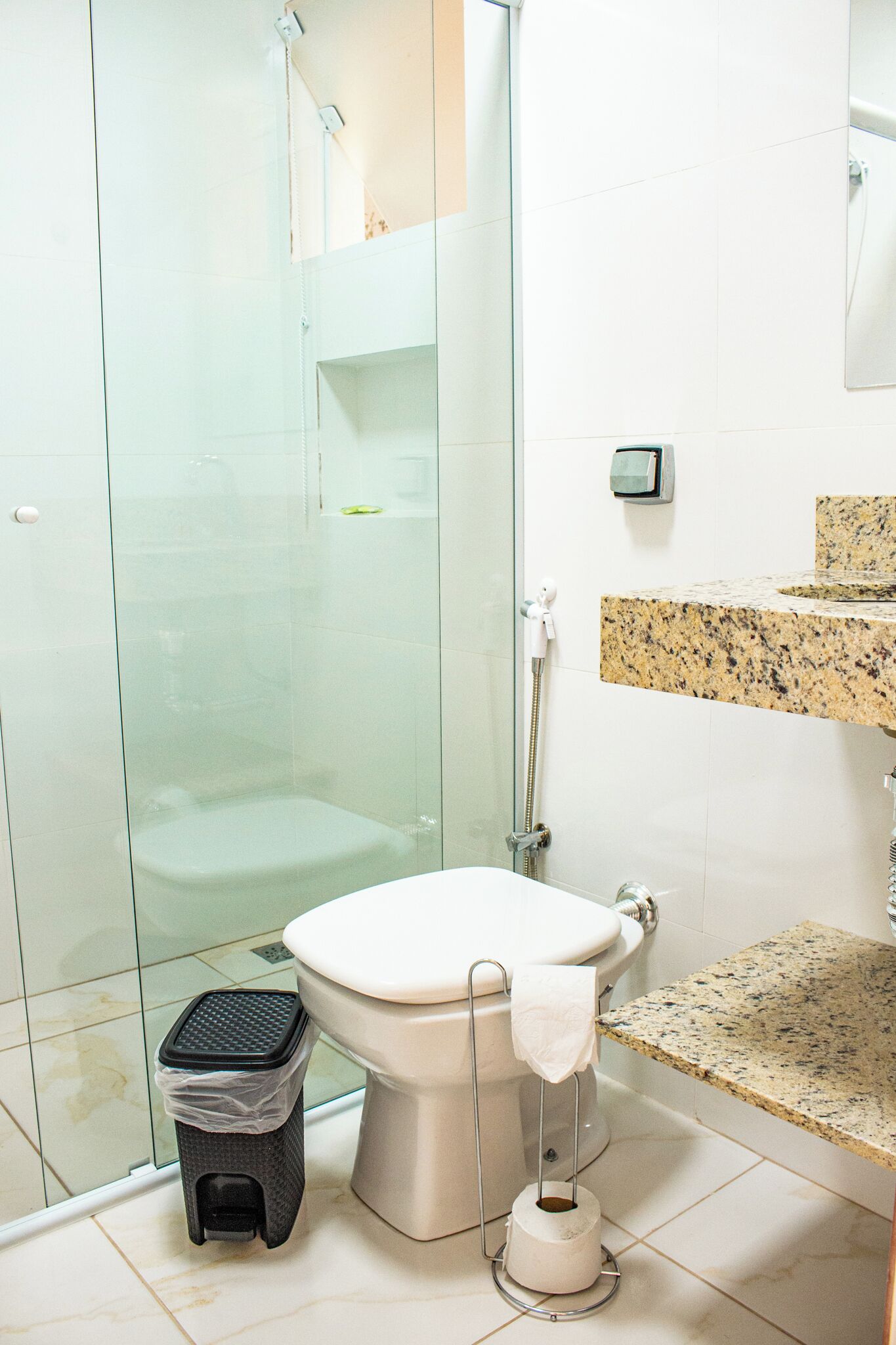 A bathroom with a glass-enclosed shower, a toilet, a trash bin, and a marble countertop.