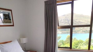Hotellihuone, jossa on sänky, yöpöytä, lamppu, ikkuna, josta avautuu näkymä järvelle ja kukkuloille, sekä seinällä oleva kehystetty kuva.