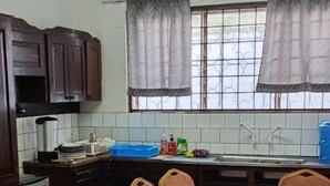 Een keuken met een eettafel bedekt met een rode tafelkleed, vier stoelen, een koelkast en een raam met gordijnen.