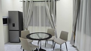 Un comedor con una mesa redonda y cuatro sillas, un refrigerador y cortinas translúcidas.