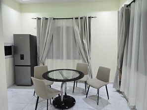 Ein Essbereich mit einem runden Tisch, vier Stühlen, einem Kühlschrank und durchscheinenden Vorhängen.