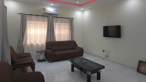 Una sala de estar con sofá, sillones, mesa de centro, televisor y equipo de aire acondicionado.