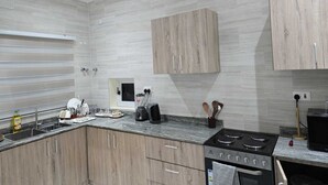 Una cocina moderna con baldosas grises, armarios de madera, una estufa empotrada y un ventanal con persianas.