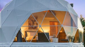Struttura a cupola geodetica con interno visibile che include un letto, una scrivania e una sedia.
