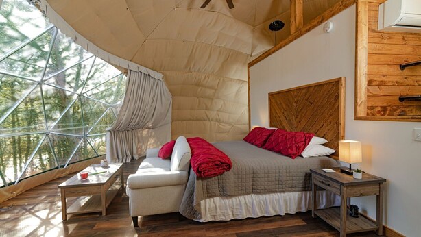 Una camera accogliente con un letto, un comodino in legno, una lampada e vista attraverso un'ampia finestra.