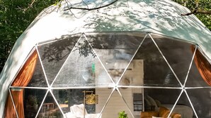 Struttura a cupola geodetica con facciata in vetro, arredi interni e vista sul paesaggio circostante.