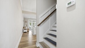 Een trap met houten treden en een leuning, die leidt naar een kamer met een witte muur en een thermostaat.
