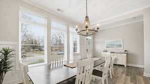Een eetgedeelte met een grote tafel, witte stoelen en een kroonluchter.