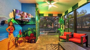 A room with a television, a ceiling fan, a pool, and red cushioned seating. - Resort Home with Pool and Spa, Game Room, Near Disney (Kissimmee)