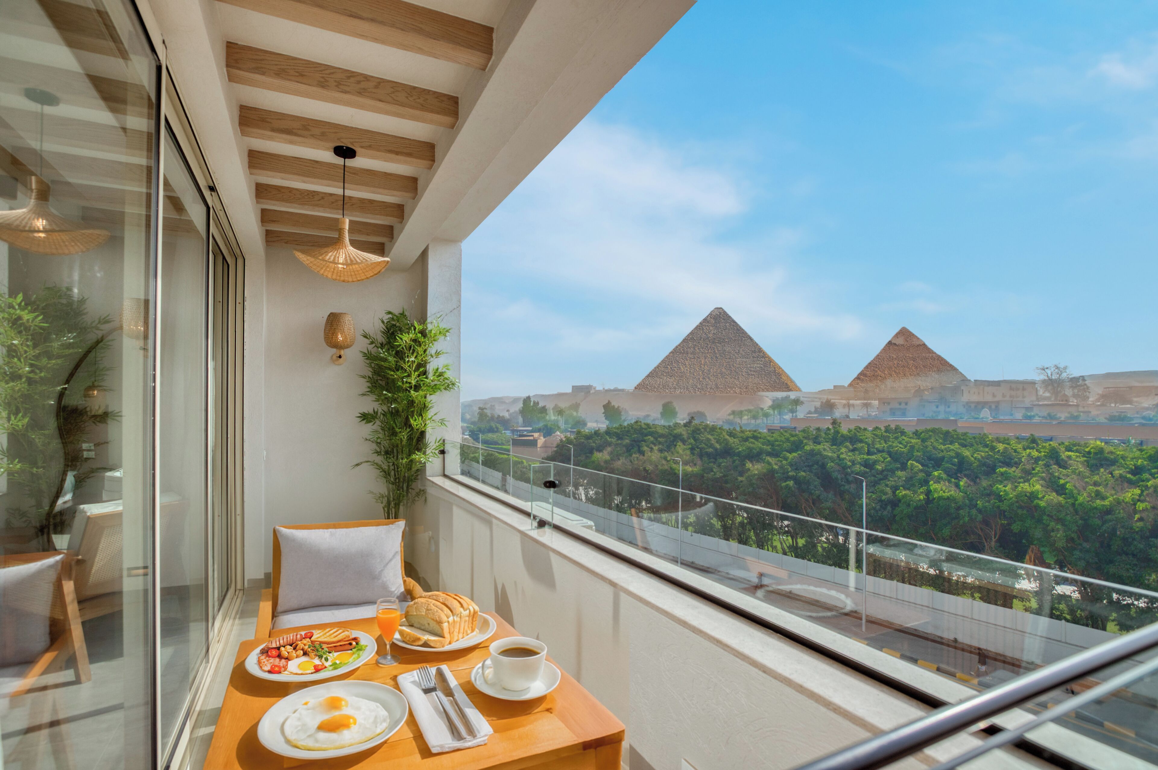 A balcony with a table set for breakfast, overlooking a view of pyramids and greenery.