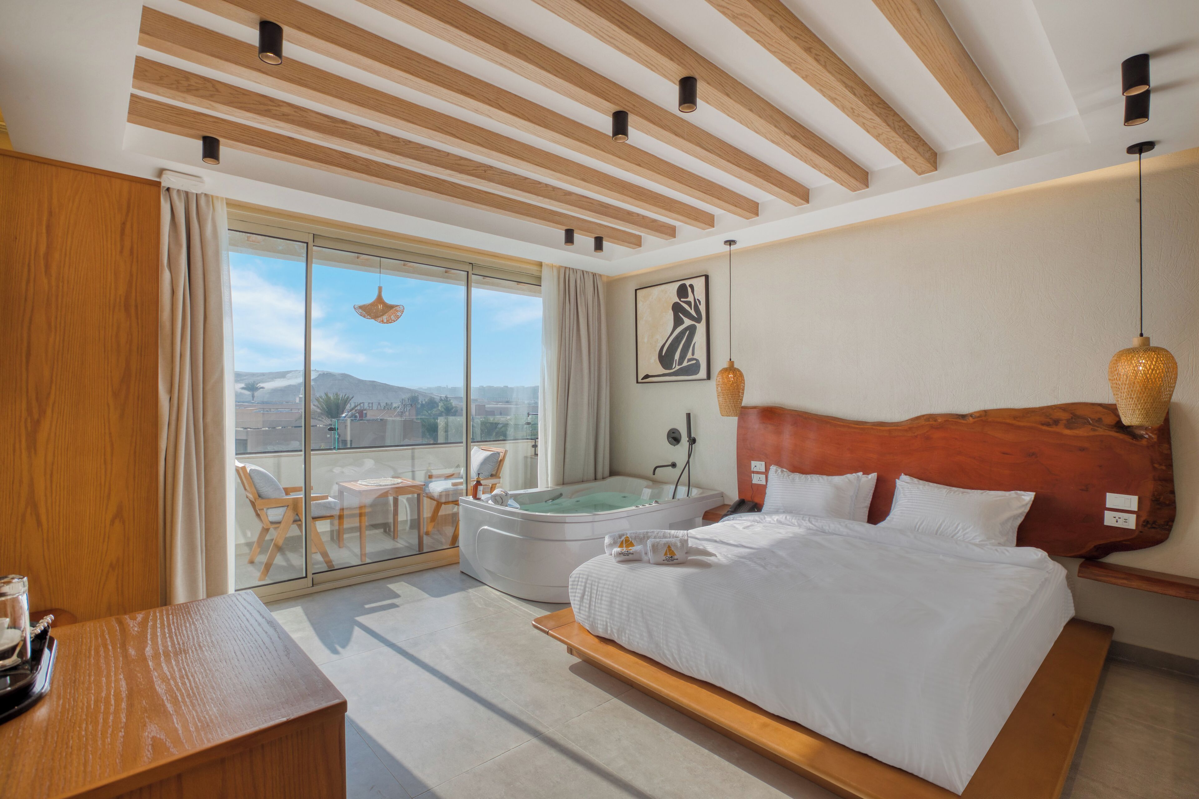 A modern hotel room with a large bed, a separate sitting area with a view, a jacuzzi, and a balcony.