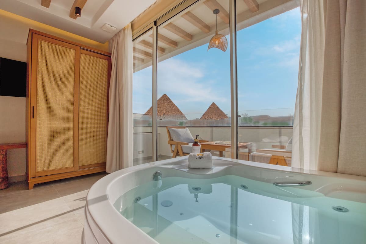Une salle de bain moderne avec un jacuzzi entouré de parois en verre, des meubles en bois et une vue sur les pyramides.