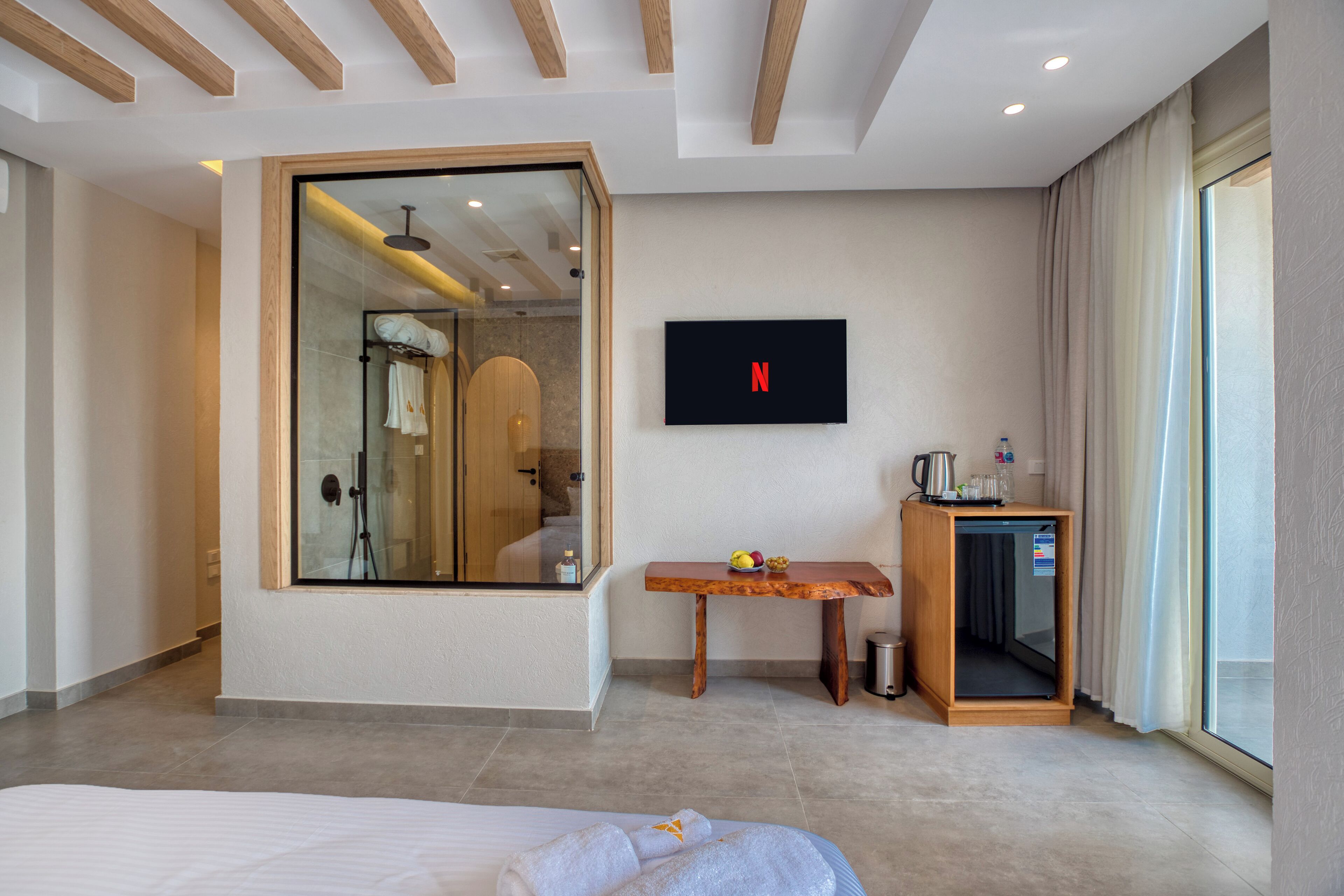 A modern hotel room with a large mirror, a TV, a wooden table with fruits, and a bed with towels.