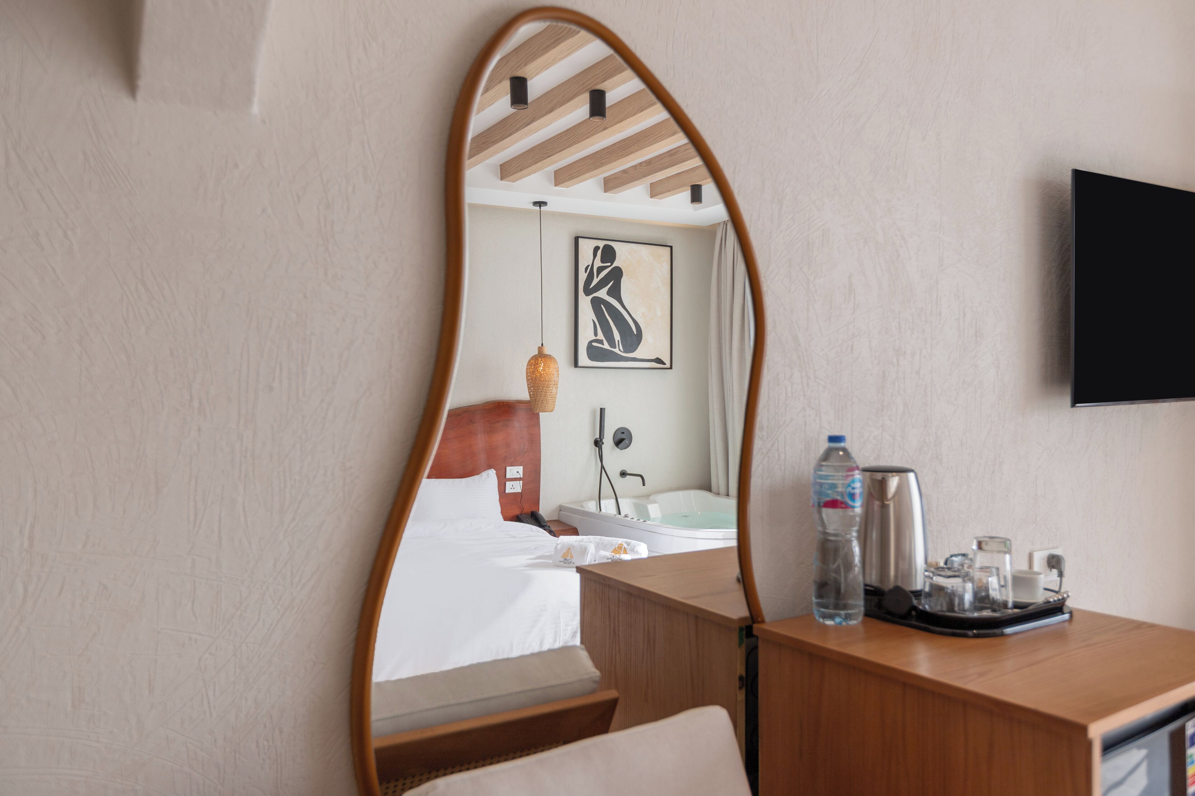 A hotel room with a bed, a wooden desk, a mirror, a TV, a bathroom with a bathtub, and a towel rack.