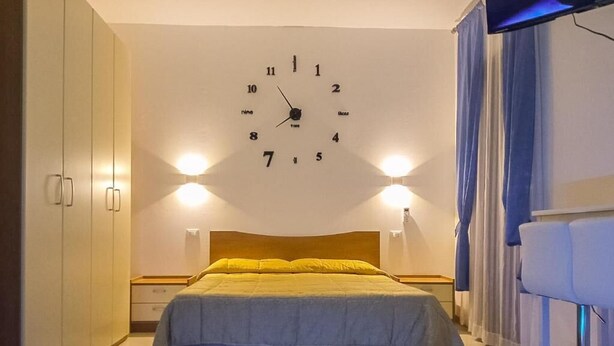 Ein Schlafzimmer mit einem Bett, einer Wanduhr, Nachttischlampen und einem Fernseher.