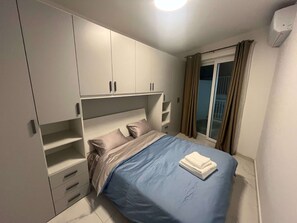 A bedroom with a bed, built-in wardrobe, and a sliding glass door to the balcony. - Qawra Seaside Birch Leaf (San Pawl il-Baħar)