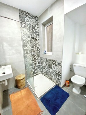 A bathroom with a shower, toilet, sink, patterned tiles, and a small window. - Qawra Seaside Birch Leaf (San Pawl il-Baħar)