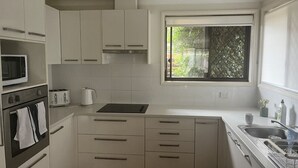 Une cuisine moderne avec des meubles blancs, un four à micro-ondes, un grille-pain, une bouilloire et un évier.