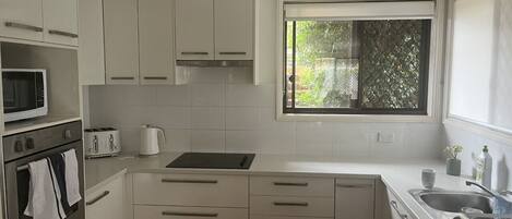 A modern kitchen with white cabinets, a microwave, toaster, kettle, and a sink.