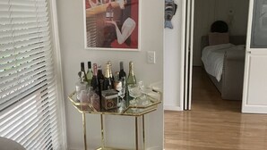 Une pièce avec une table en verre sur laquelle sont disposées différentes bouteilles et différents verres, une affiche accrochée au mur et un lit à l’arrière-plan.